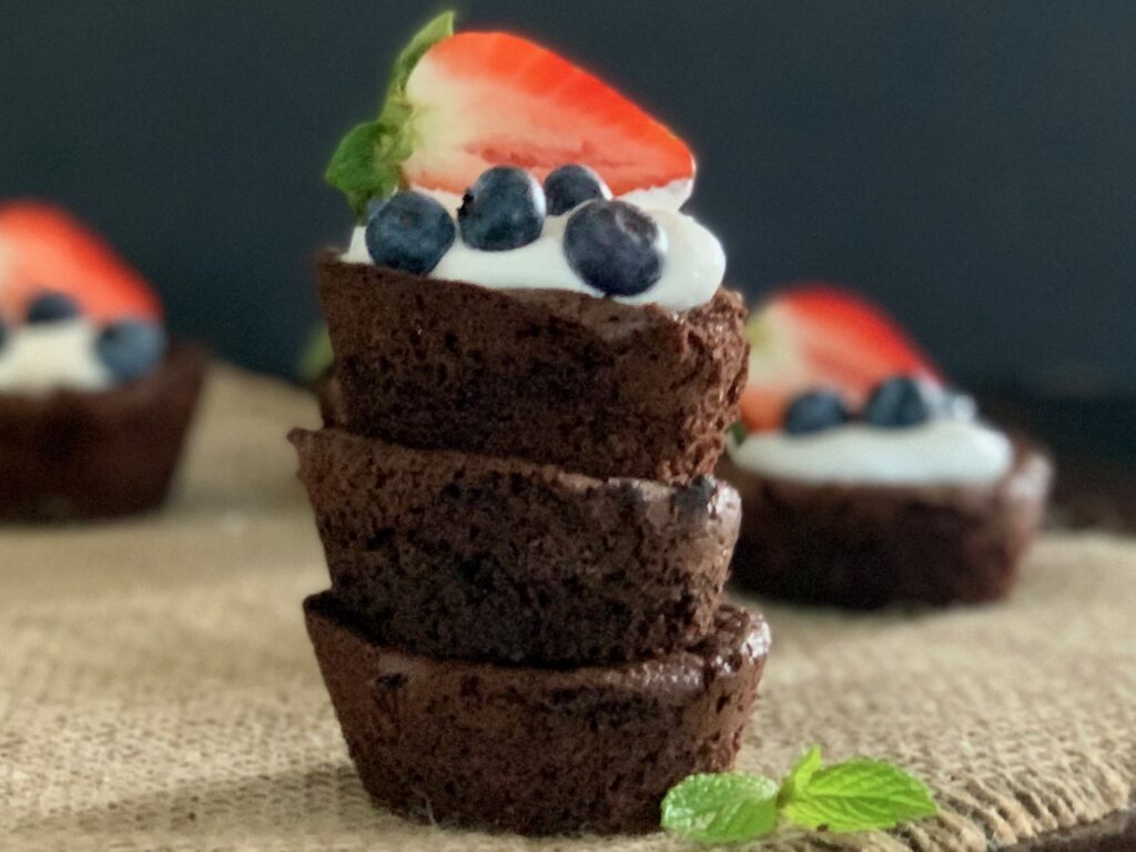 A stack of homemade brownie bites topped with whipped topping and fruit.