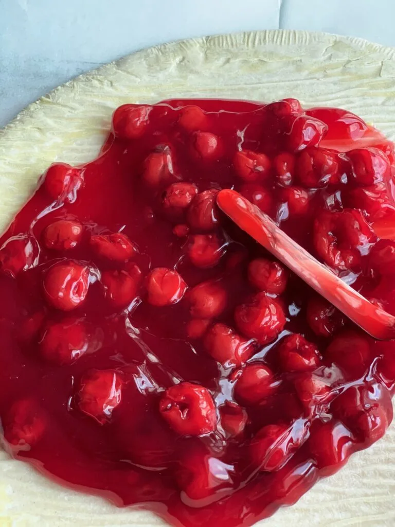 spreading cherry pie filling on a pizza crust