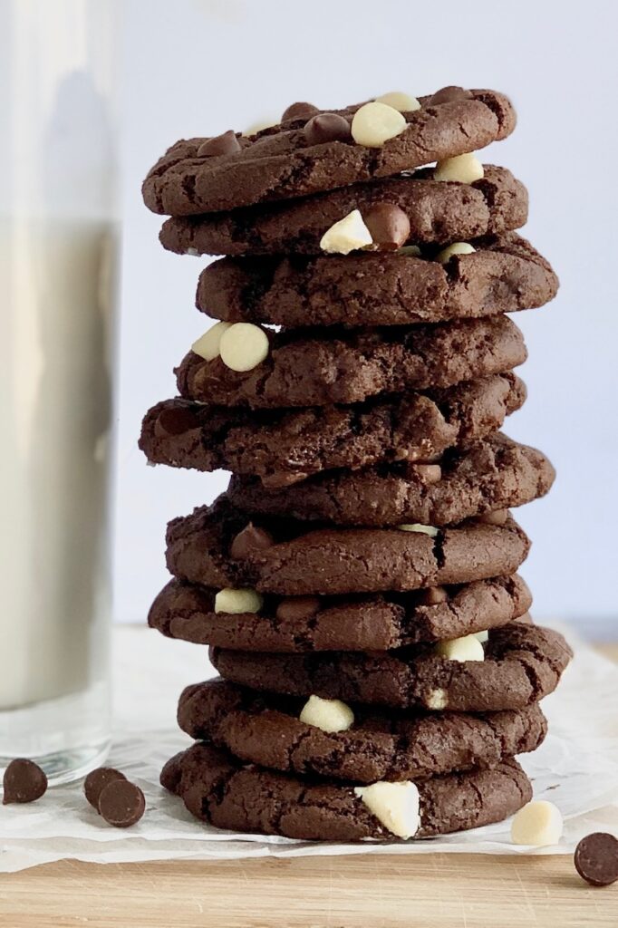 Several white chocolate chip cookies stacked next to glass of almond milk.