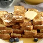 French toast sticks on a serving plate with dairy free butter and powered sugar.