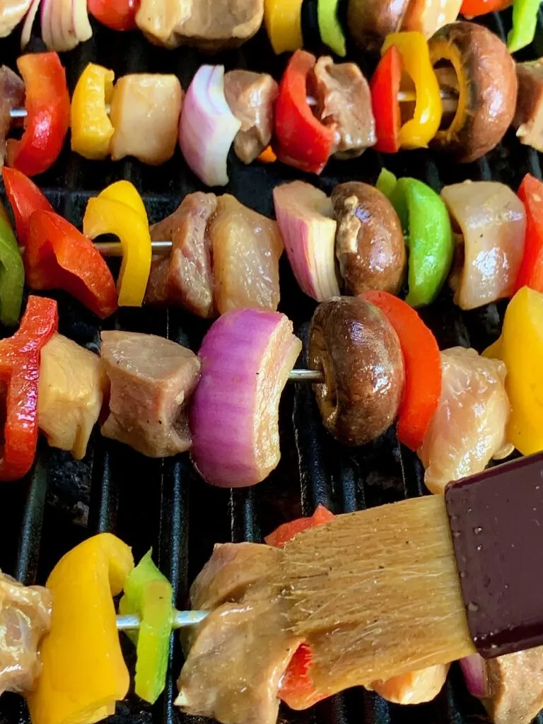 Shish Kabobs on the grill with a basting brush applying more marinade