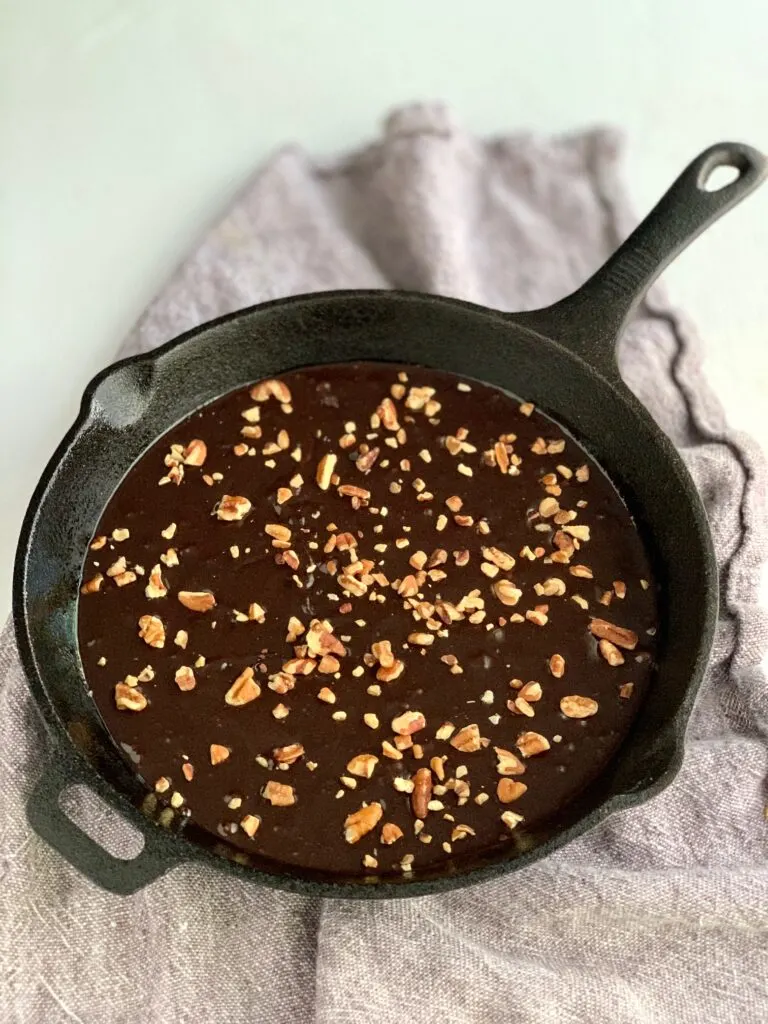 Brownie batter in a cast iron skillet with chopped walnuts on top