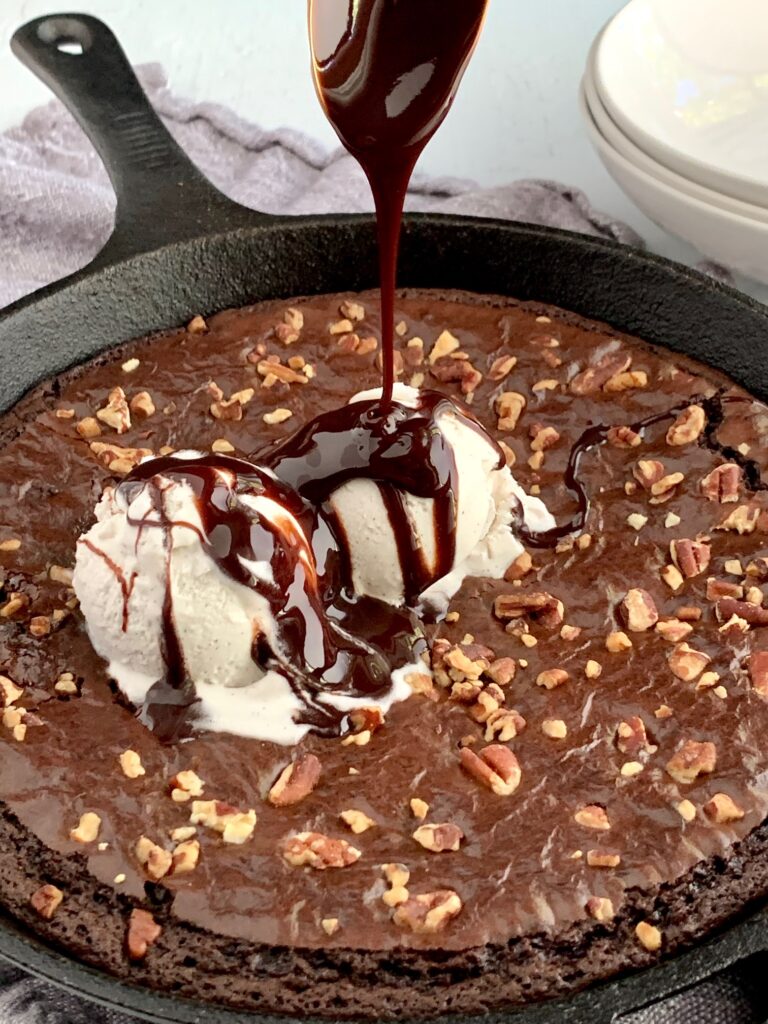 Baked brownie in a skillet with walnuts, ice cream, and chocolate syrup.