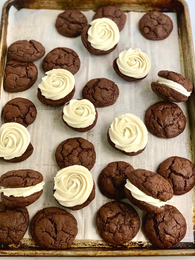 A baking sheet pan of buttercream frosting sandwiched between fudgy brownie cookies.