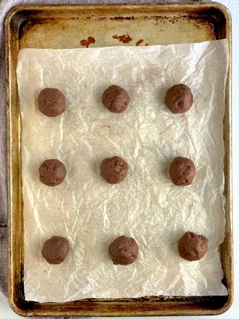 9 balls of brownie cookie batter on a baking sheet with parchment paper. 