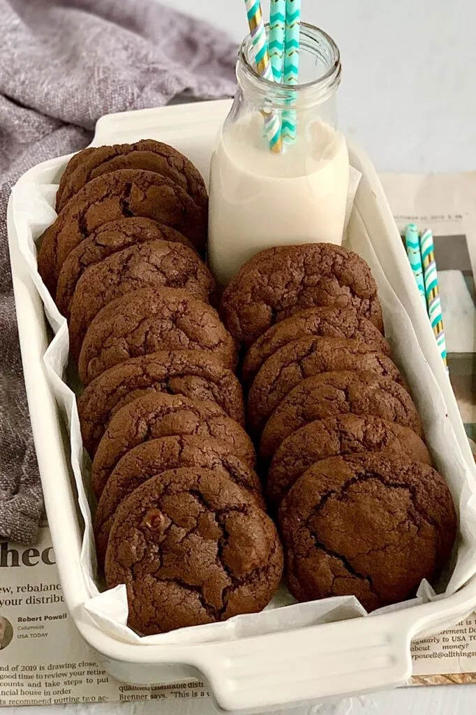 Several fudgy brownie cookies in a small baking dish with a glass of dairy free milk. 