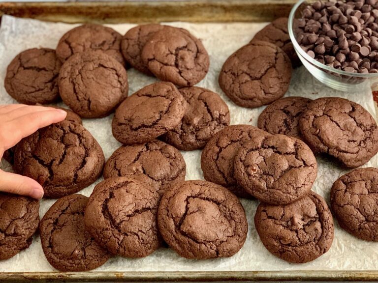 A child's hand reaching for a baking sheet full of fudgy brownie cookies.