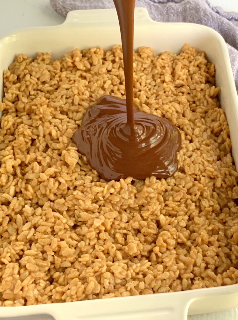 Cereal with peanut butter in a 9 x 13 inch pan with melted chocolate being drizzled on it.