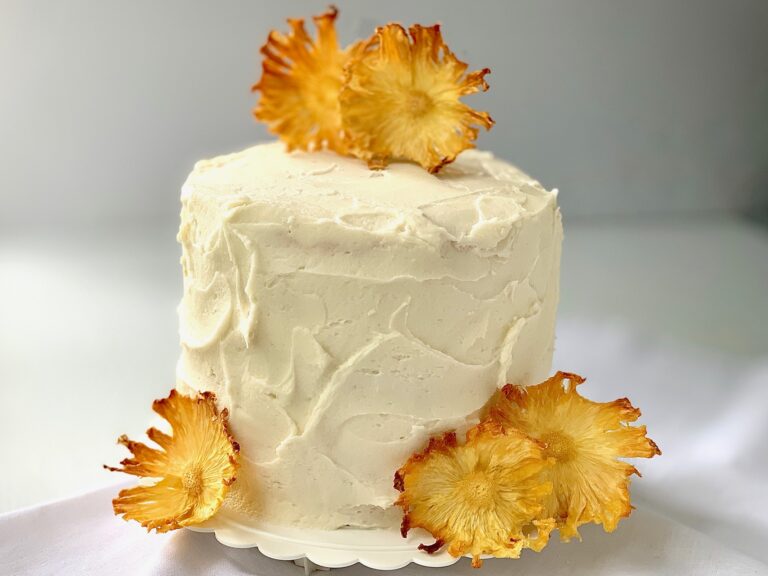 A 3 layer cake frosted with buttercream icing and garnished with dried pineapple flowers.