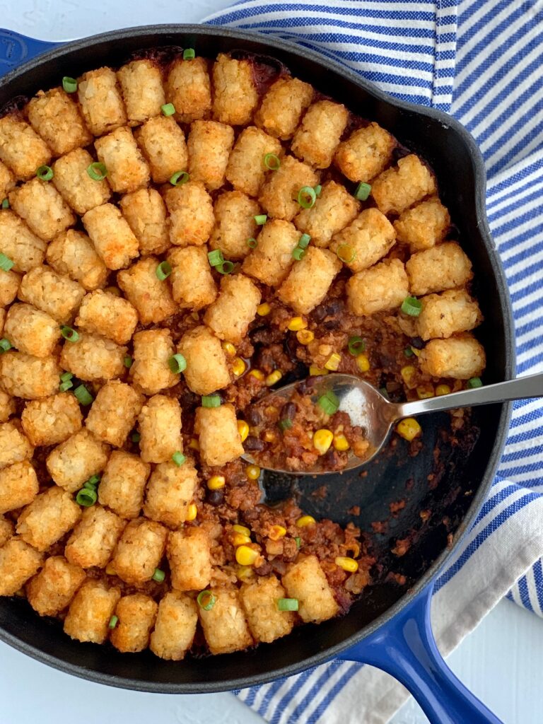 Tater tots over a taco mixture of ground beef, corn, black beans, and sauce mixtures. 