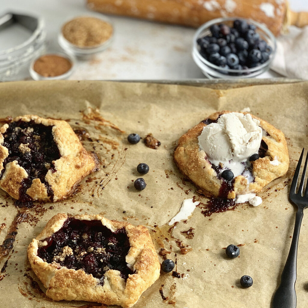 3 mini blueberry galettes and one has a dollop of ice cream on it.