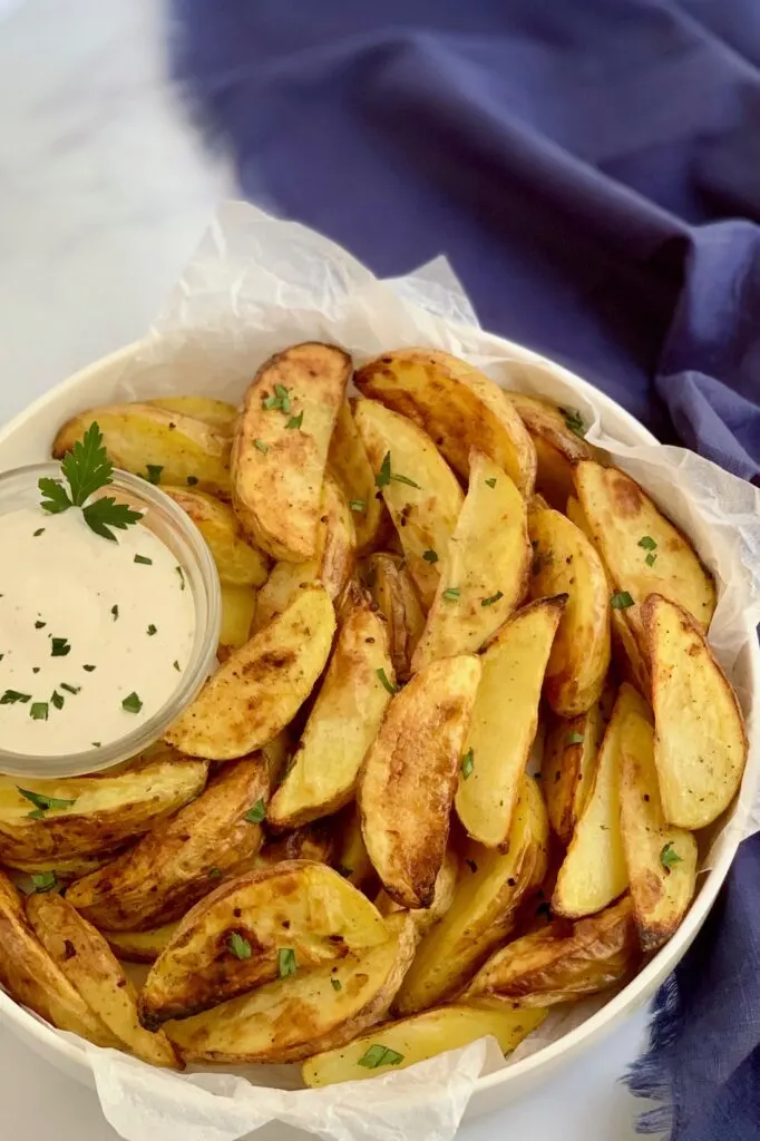 A plate heaping with baked potato wedges and dressing.