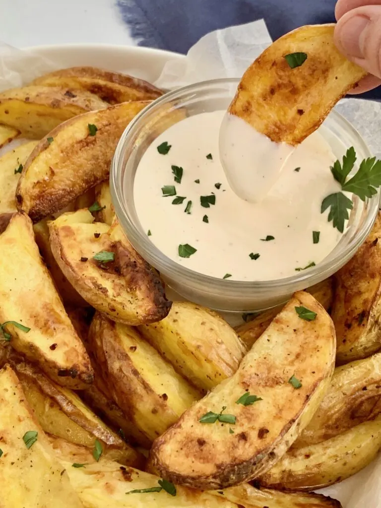 A baked potato wedge getting dipped into dairy free ranch dressing.