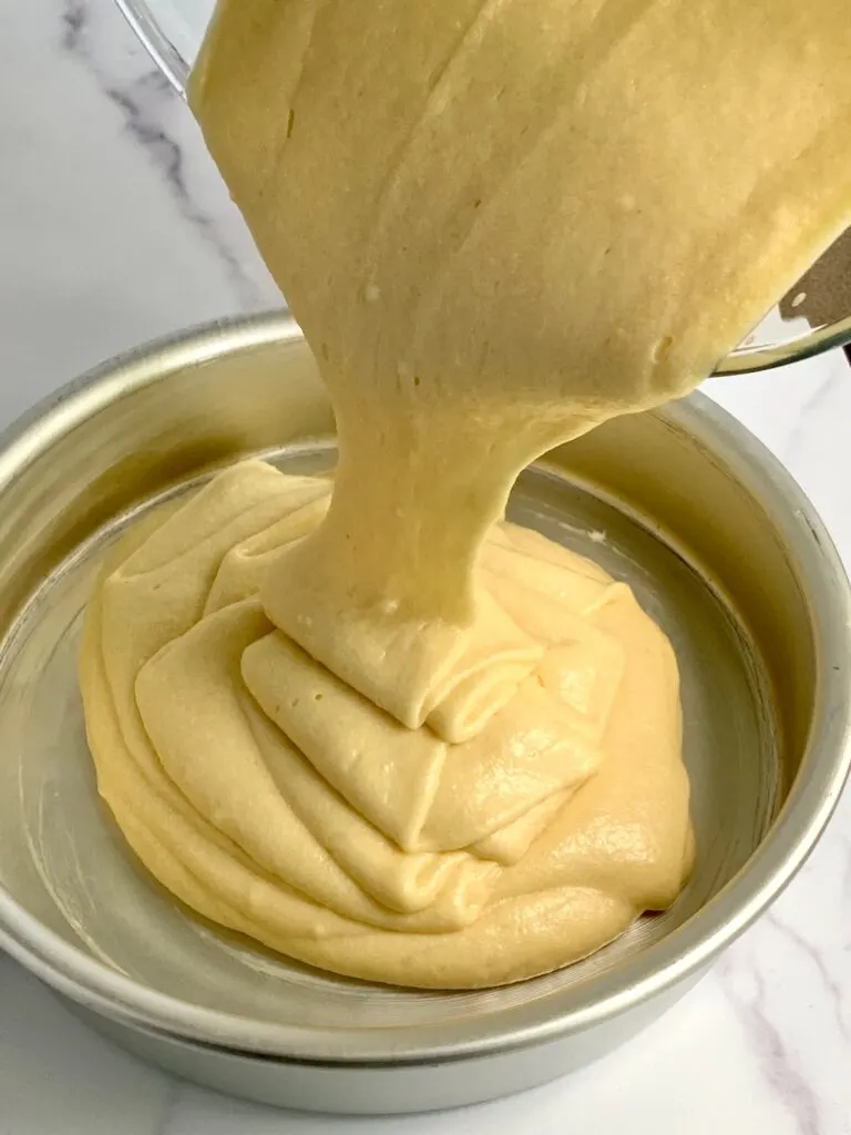 Pouring  yellow cake batter into a cake pan.