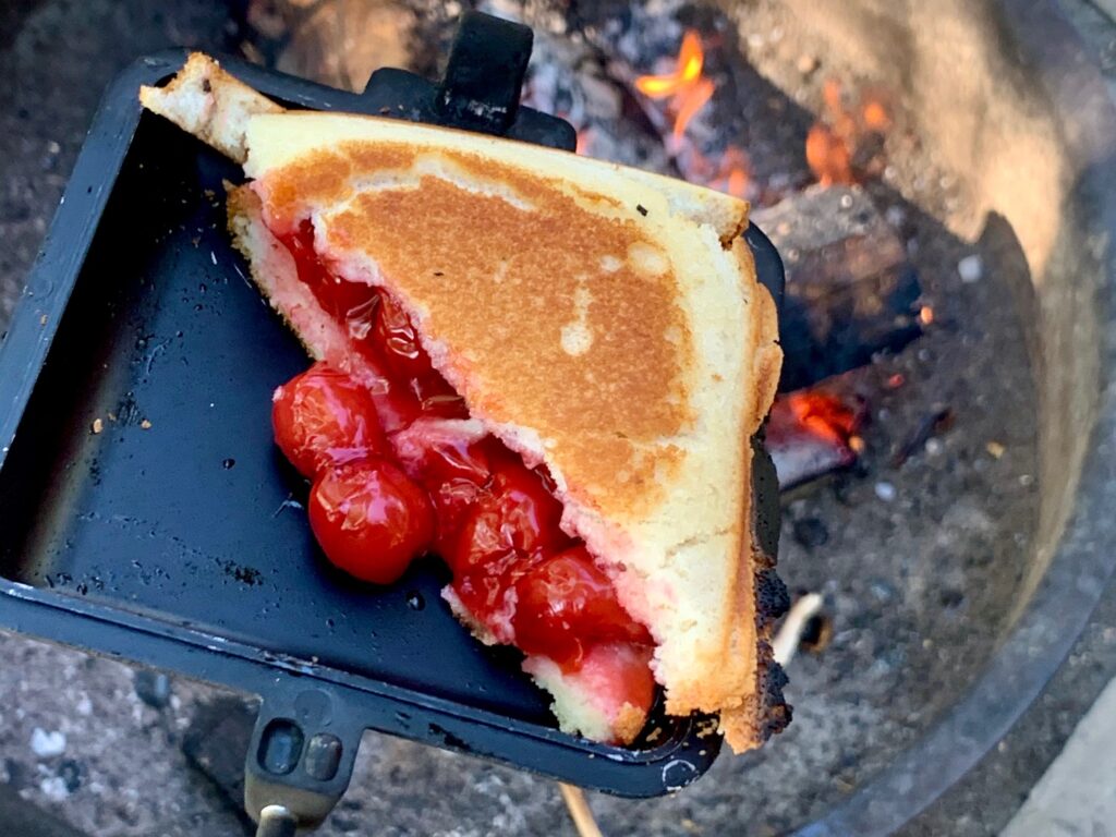 Cherry pie filling sandwiched between to slices of bread in a pie maker by the campfire. 