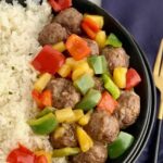 a bowl of white rice with meatballs, pineapple, and bell peppers