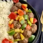 a bowl of white rice with meatballs, pineapple, and bell peppers