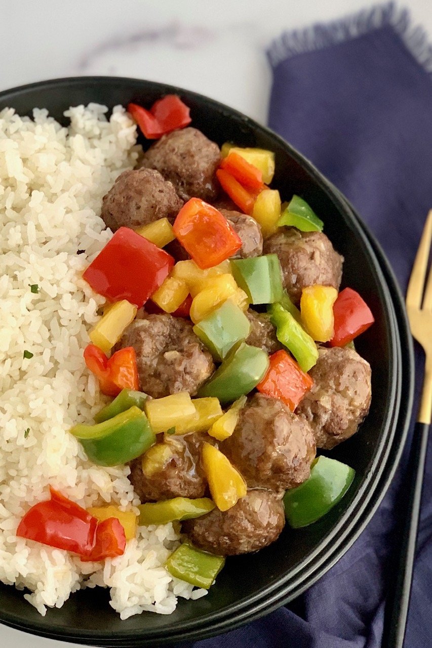 a bowl of white rice with meatballs, pineapple, and bell peppers