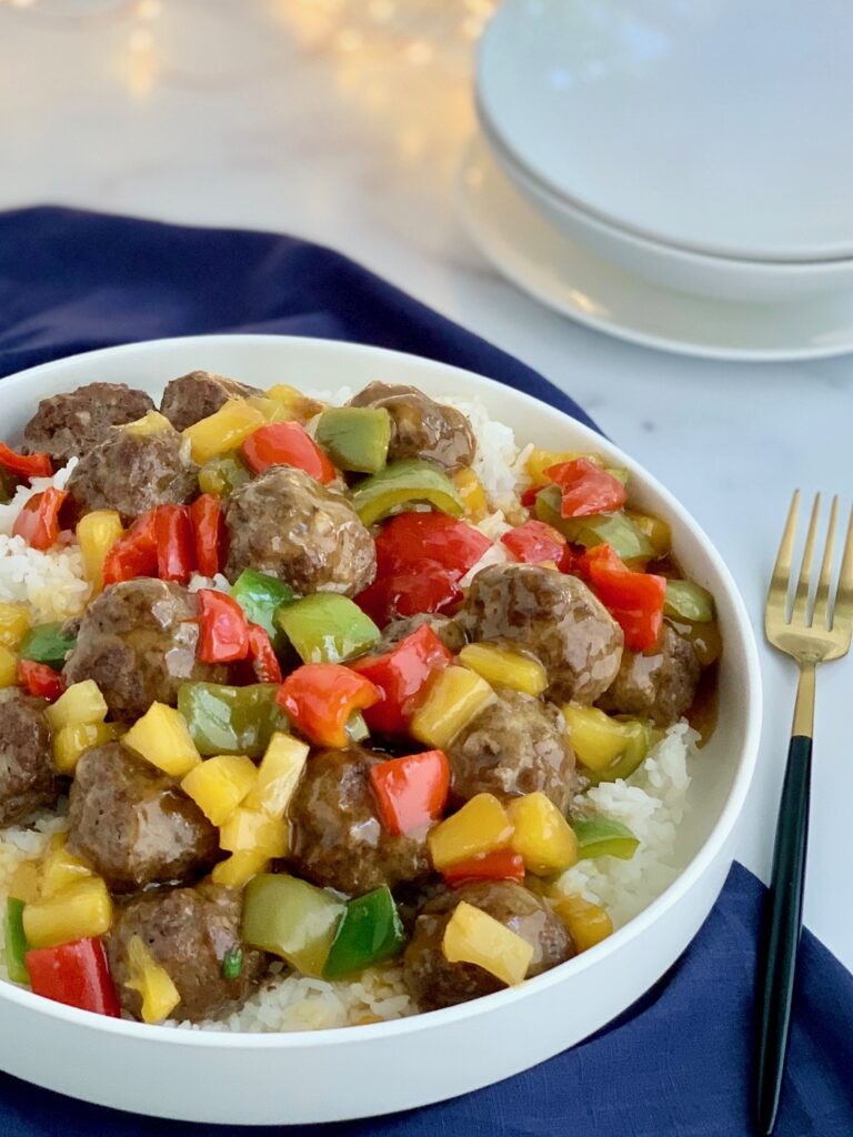 A bowl of white rice with meatballs, pineapple chunks, and bell peppers. 