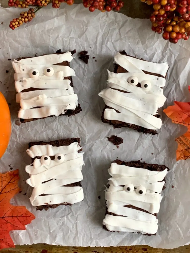 4 rectangle brownies with white frosting zig zagging back and forth and googly eyes making them look like mummies