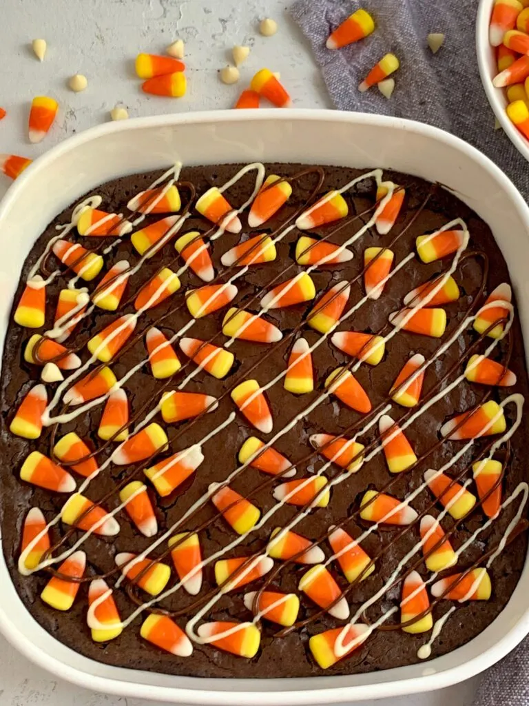 a large plate of brownies with candy candy corns on top of them and chocolate drizzle