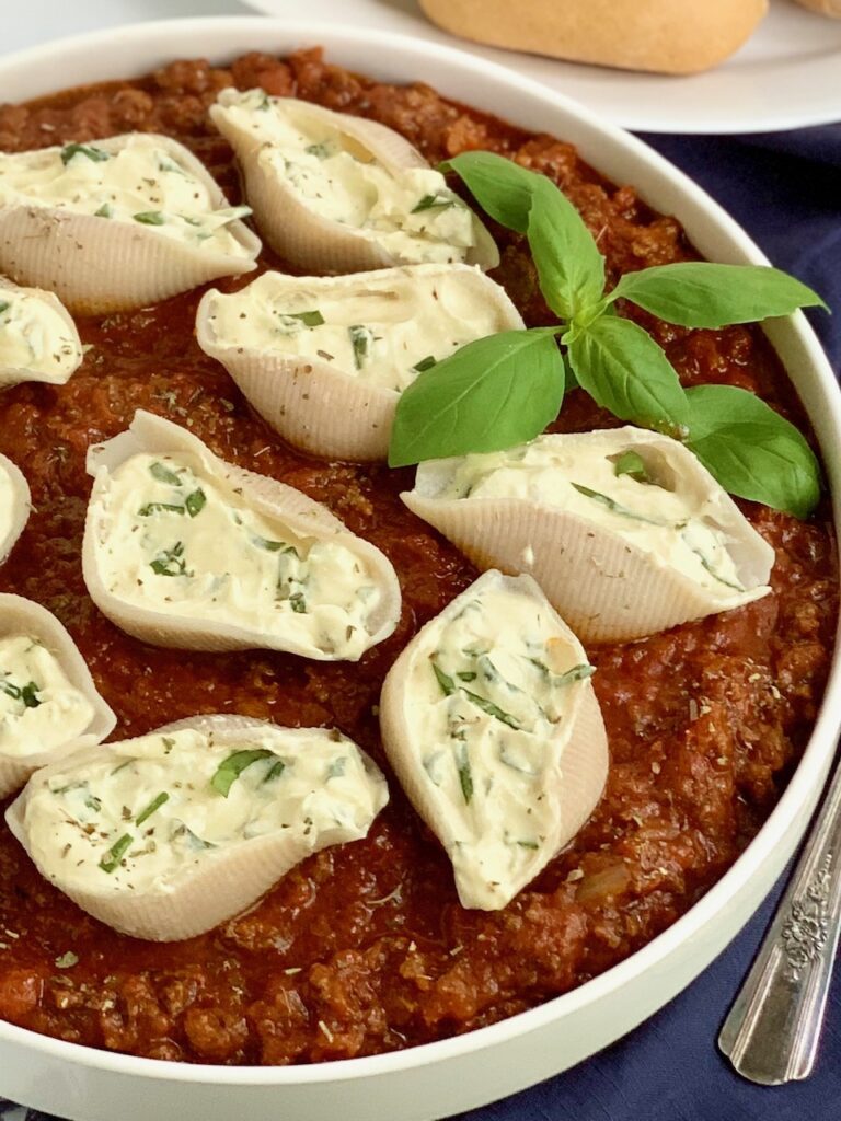 A large baking bowl of meat sauce and ricotta stuffed shells. 