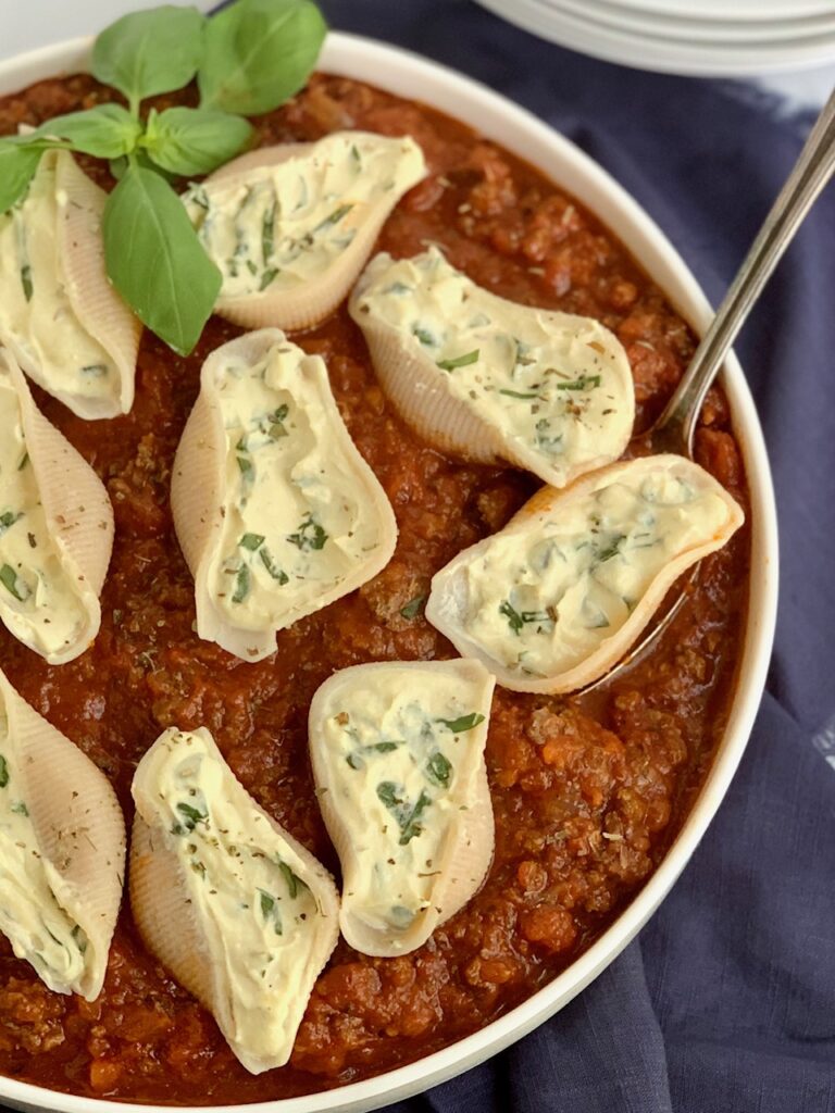 A large baking bowl of pasta sauce and shells filled with ricotta and spinah. 