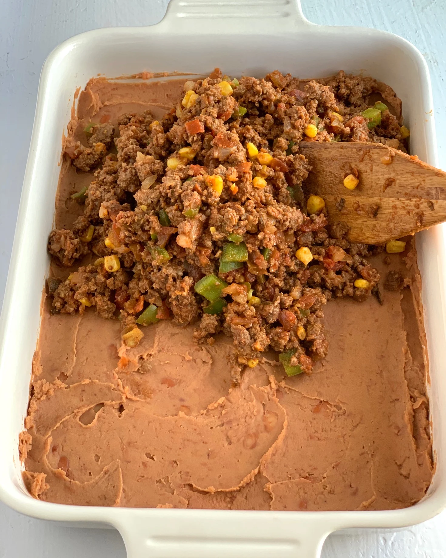 A baking dish filled with a layer of refried beans and taco meat sauce.