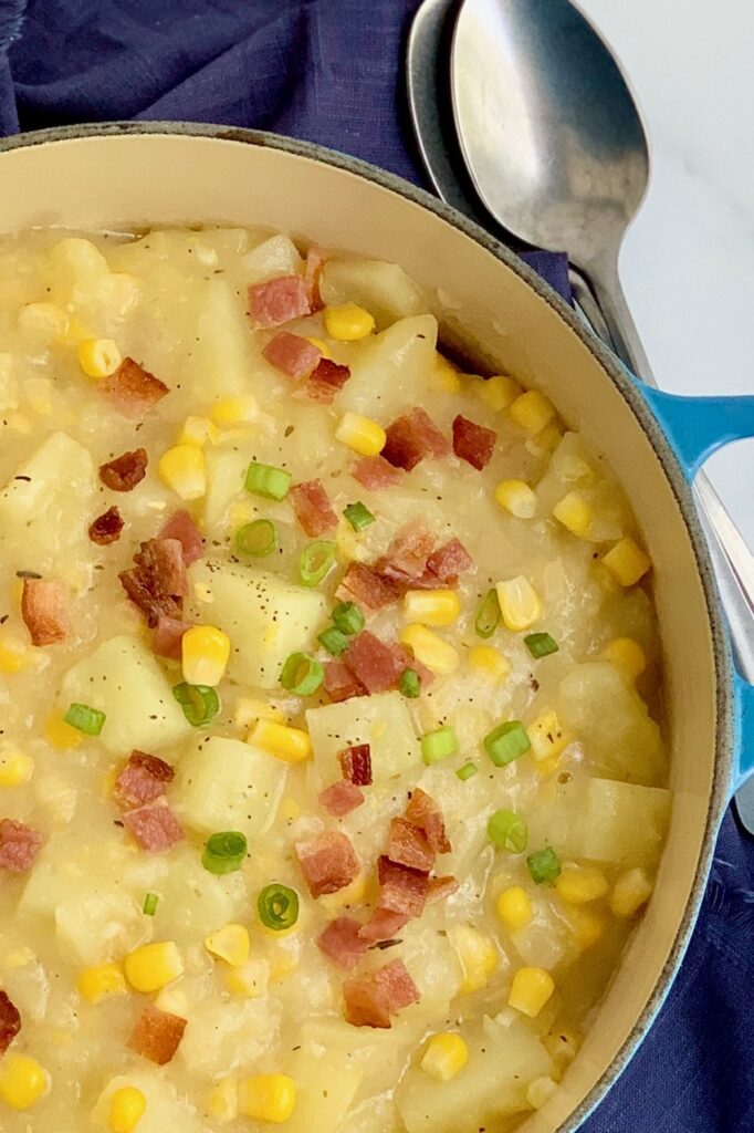 A bowl full of creamy potato corn chowder topped with bacon and green onions.