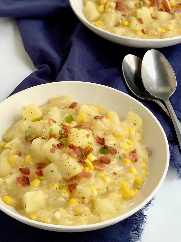 A bowl full of creamy potato corn chowder topped with bacon and green onions.