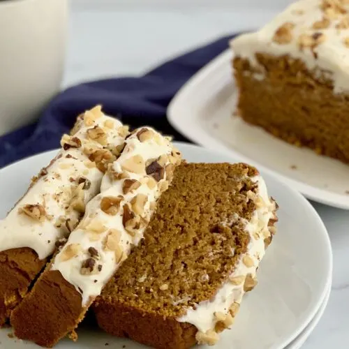 Slices of pumpkin bread with cream cheese frosting on top with crushed walnuts.