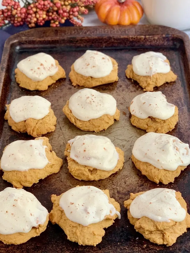 a baking tray of pumpkin cookies with cream cheese on top