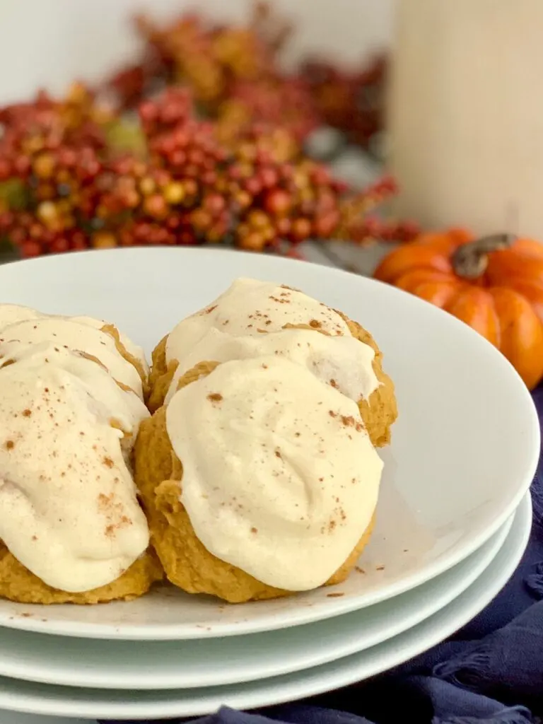 A plate of pumpkin cookies with cream cheese frosting and a dusting of cinnamon