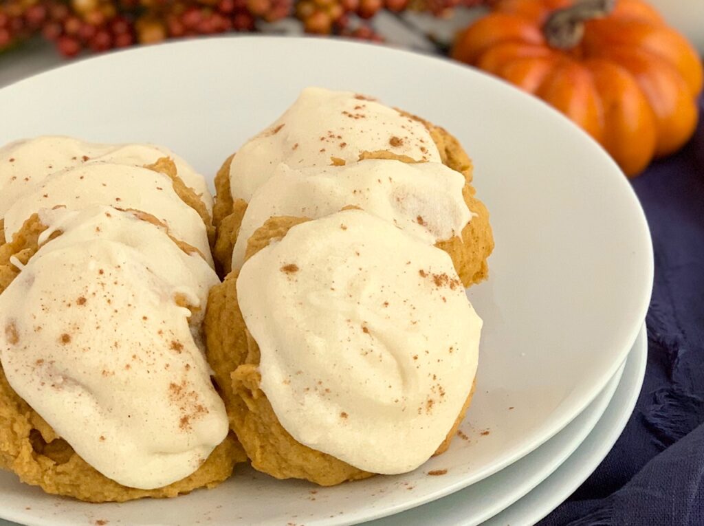 A plate full of pumpkin cookies with cream cheese frosting.