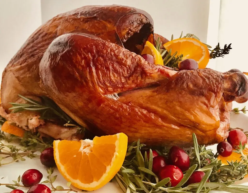 A smoked turkey on a serving platter with fresh sliced oranges, cranberries, and herbs.