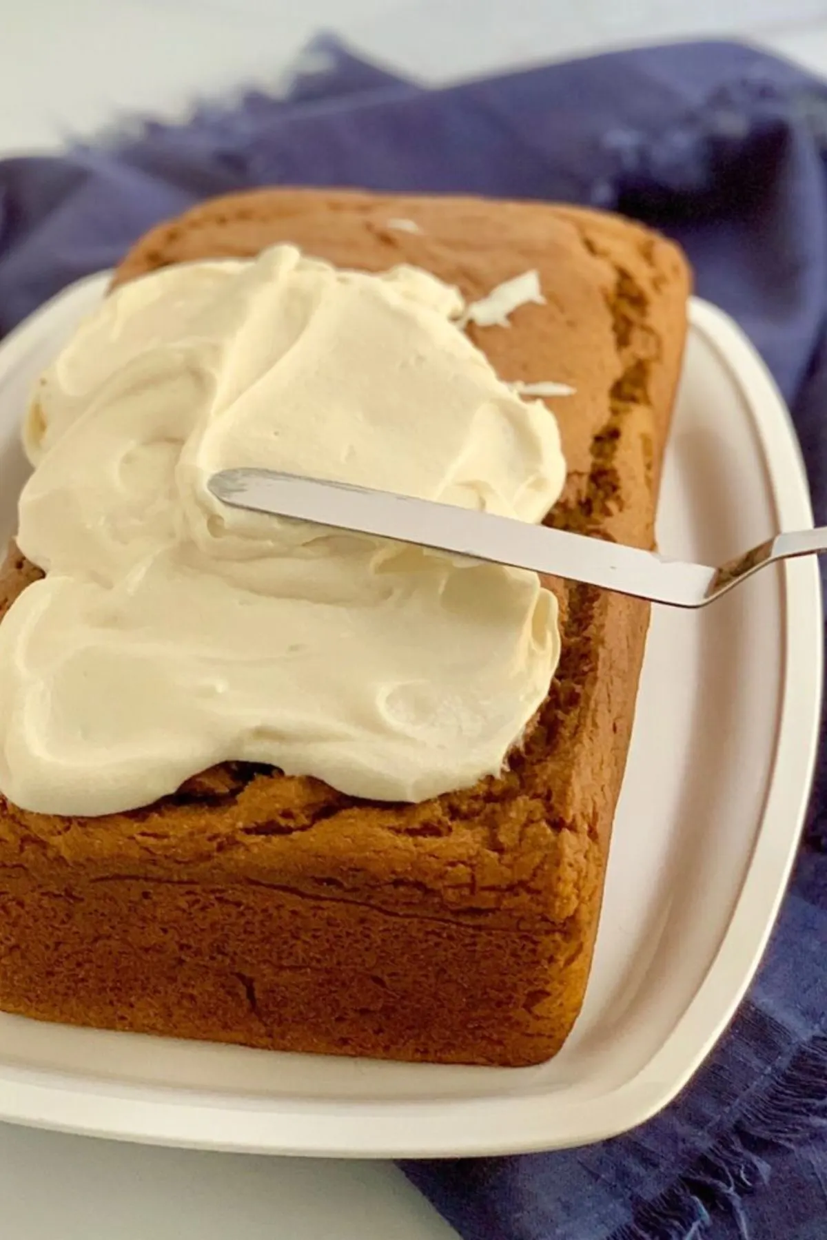 An angled spatula spreading out the dairy free cream cheese on pumpkin bread.