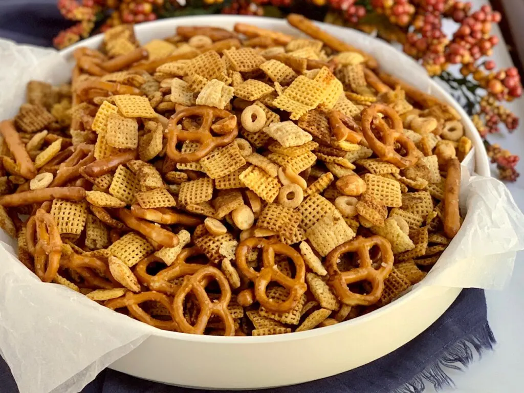 a large party bowl of chex party mix that has pretzels, peanuts, chex mix, and corn mix.