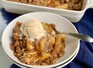 A bowl of sliced apples topped with a ooey gooey brown sugar, butter, and oatmeal mixture then with dairy free ice cream on top.