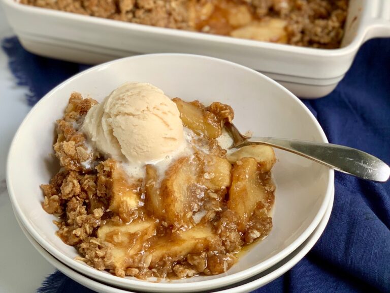 A bowl of sliced apples topped with a ooey gooey brown sugar, butter, and oatmeal mixture then with dairy free ice cream on top.