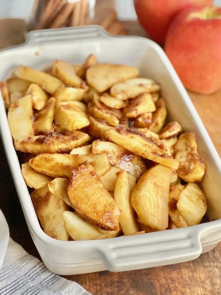 A white baking dish filled with thin apple slices and a brown sugar mixture.