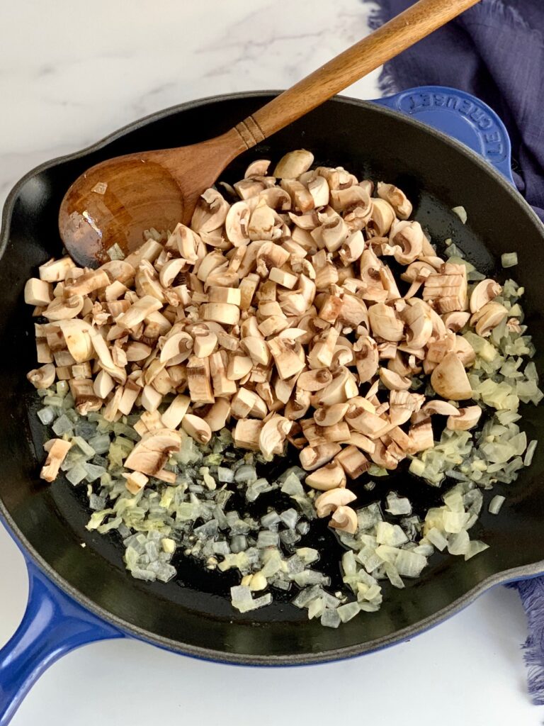 A skillet with diced onions, minced garlic, and chopped mushrooms.