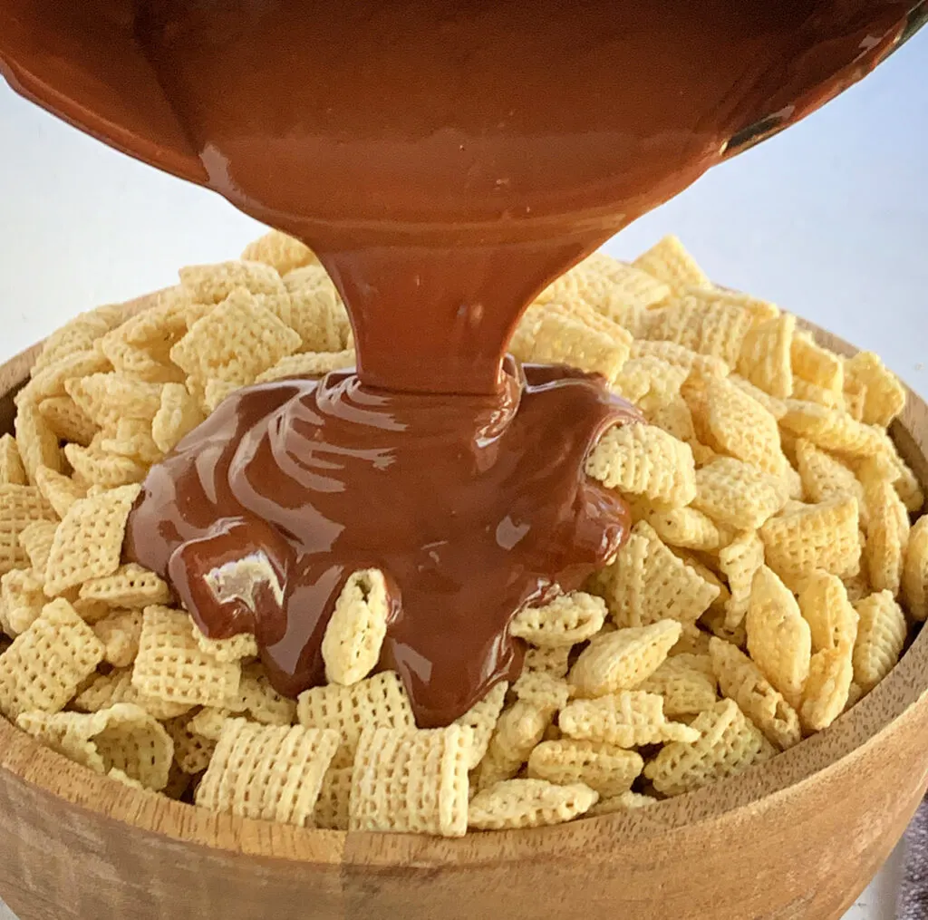 Melted peanut butter and chocolate mixture being poured onto a bowl of chex cereal.