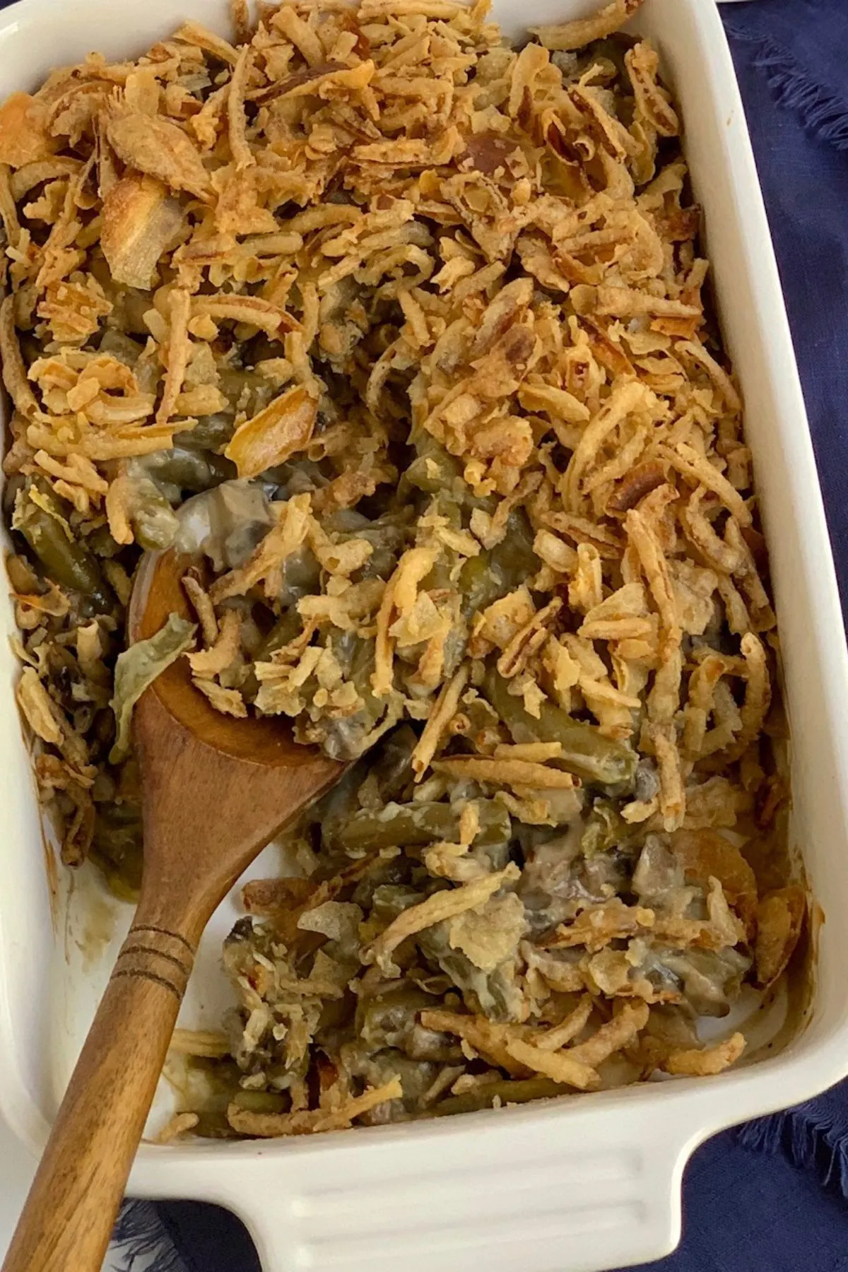 Baking dish with dairy free green bean casserole and a wooden spoon stirring it around.