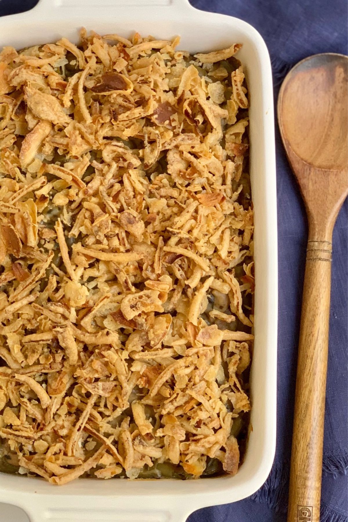 A wooden spoon next to a baking dish with gluten free green bean casserole.