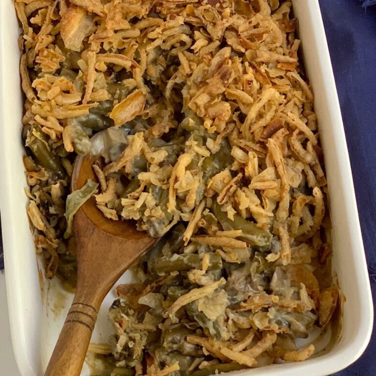 A baking dish of gluten free green bean casserole with a wooden serving spoon in it.
