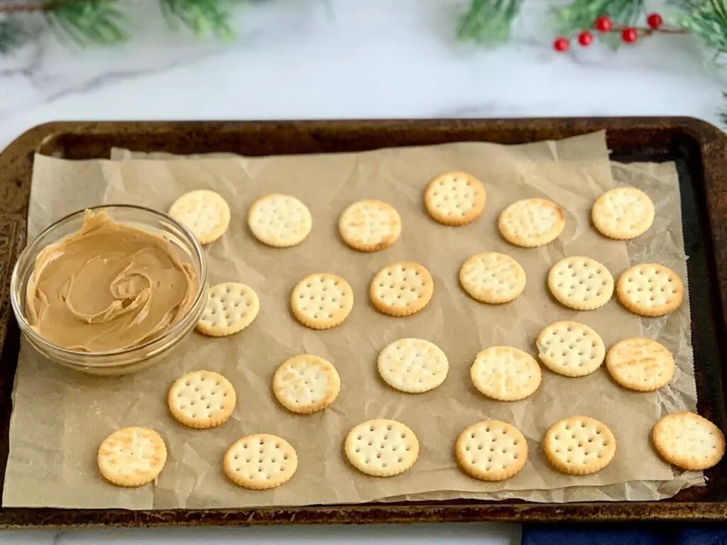 A baking sheet lined with wax paper and crackers on it.