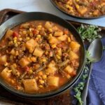 A large black bowl filled with tender potatoes, chunks of ground beef, corn, green beans, fire roasted tomato, broth, and a tomato juice combination.