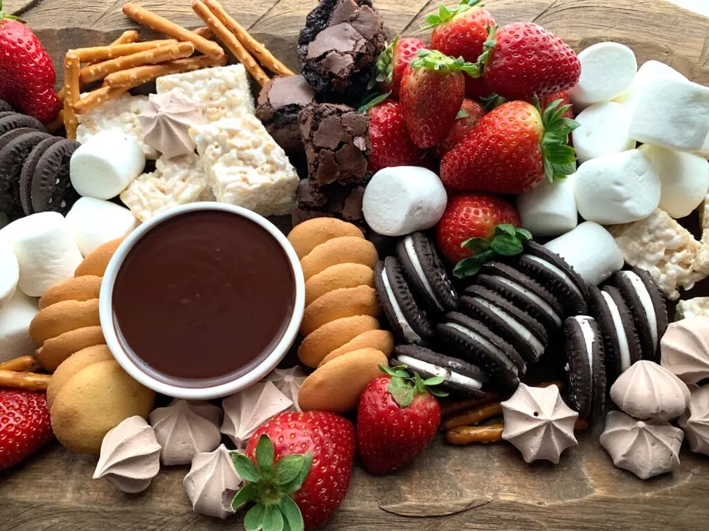 A large serving platter with oreo like cookies, vanilla wafers, strawberries, marshmallows, brownie bites, and meringue kisses.