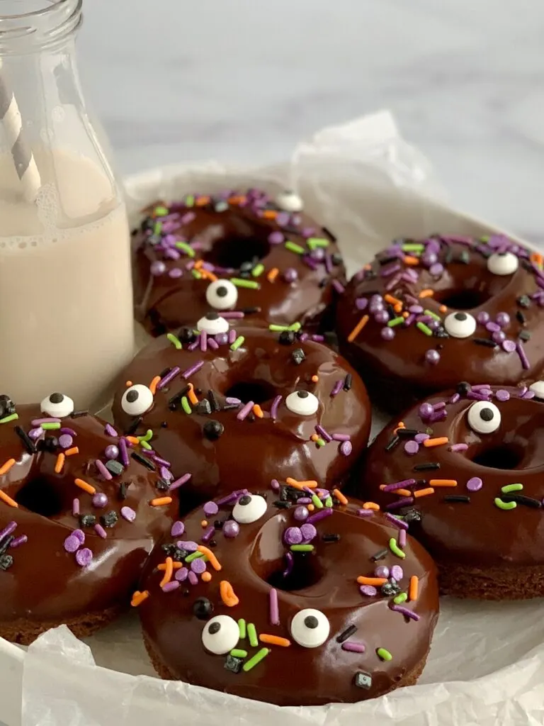 A serving plate filled with 6 double chocolate donuts topped with chocolate ganache and Halloween themed sprinkles.