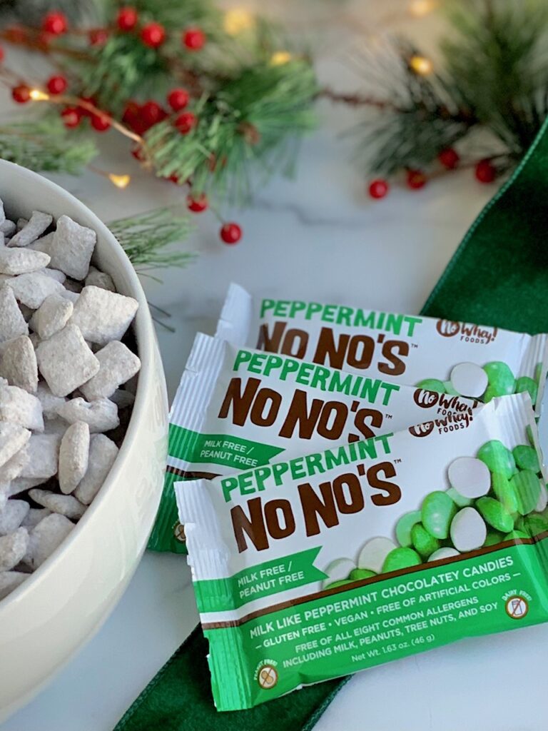 a white bowl full of traditional puppy chow next to 3 snack size bags of No Whey Foods Peppermint No No's.
